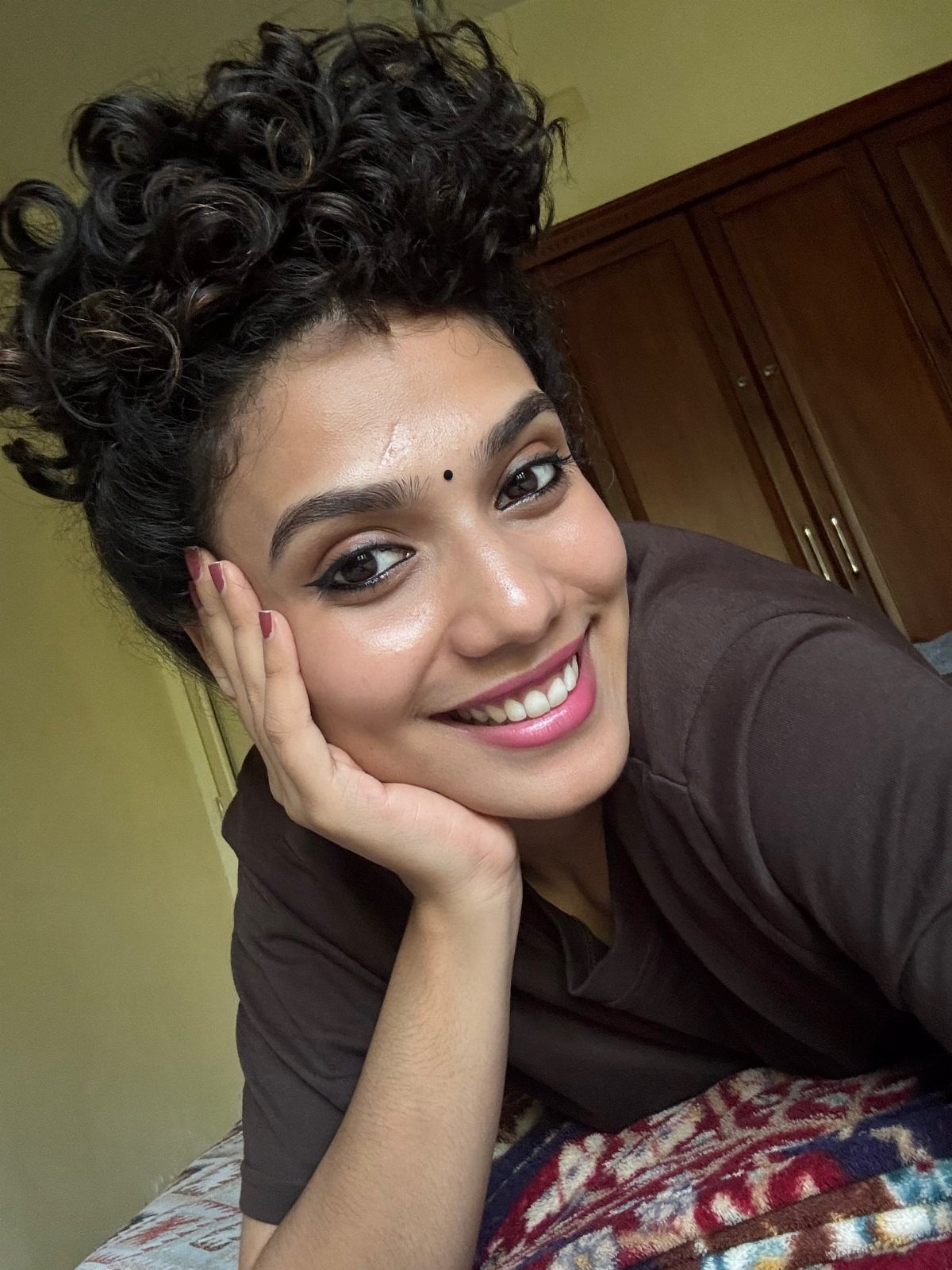Person smiles with dark curls gathered high on their head in a pineapple hairstyle