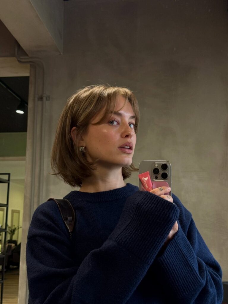 Woman with a chin-length brown bob and bangs taking a mirror selfie