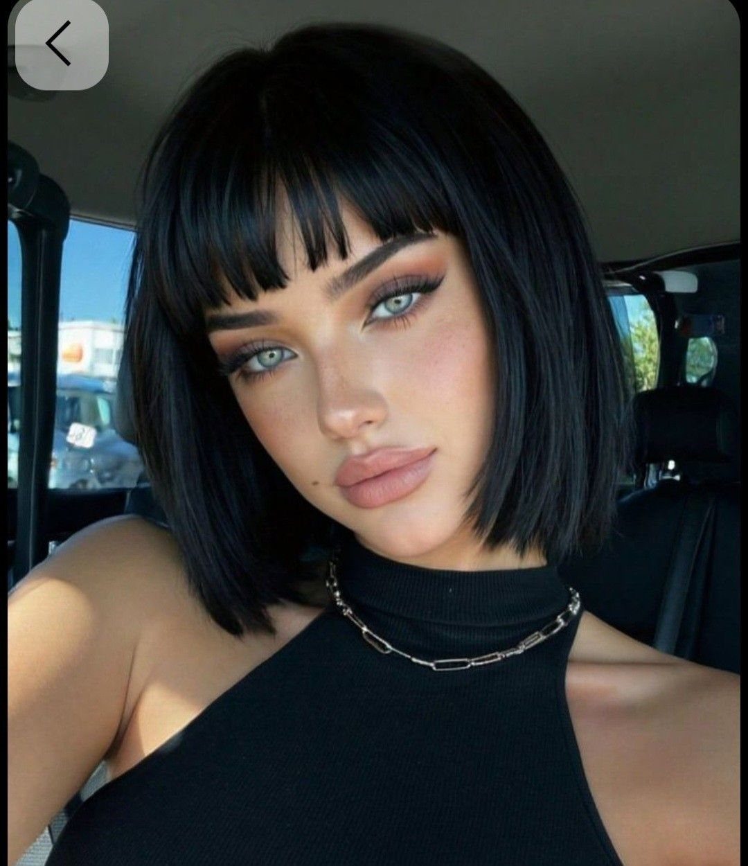 Woman showing a sleek black bob haircut with straight bangs inside a car
