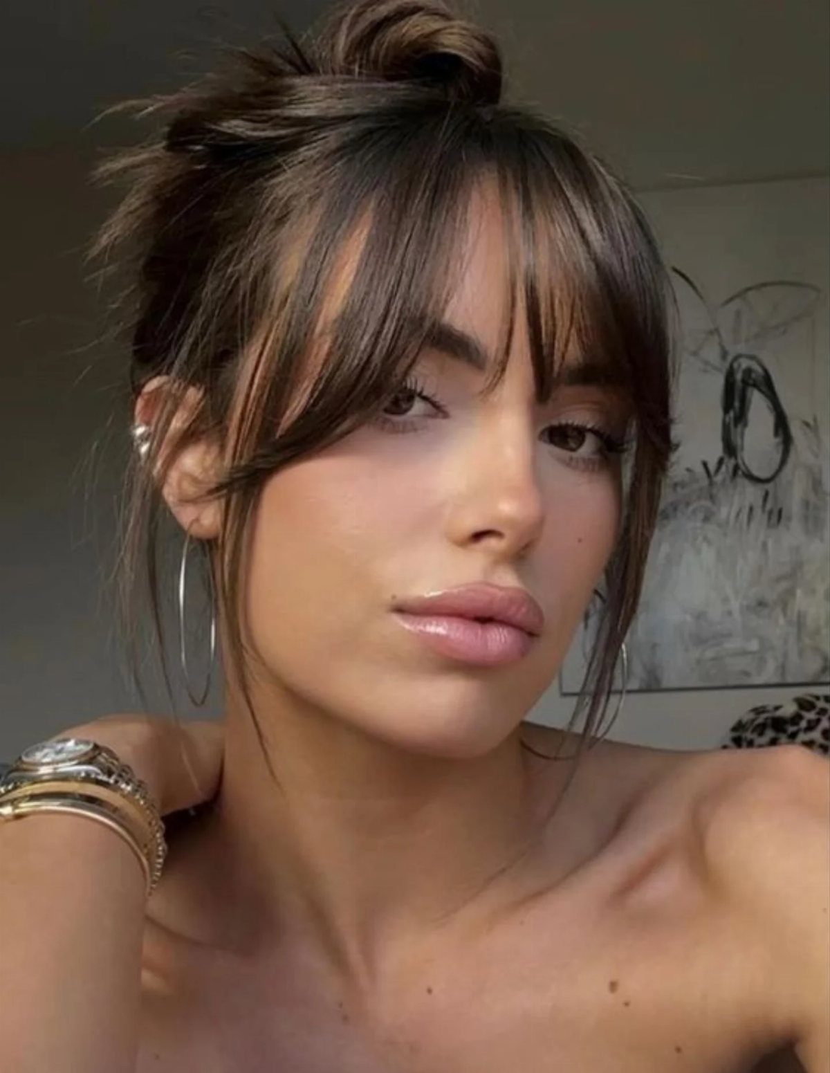 Woman with wispy bangs and a loose dark updo poses in a close-up portrait