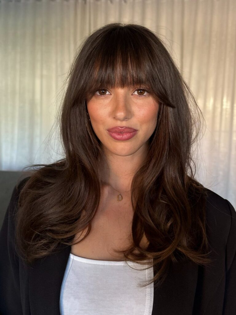 Woman with long wavy dark hair and soft, full Birkin bangs