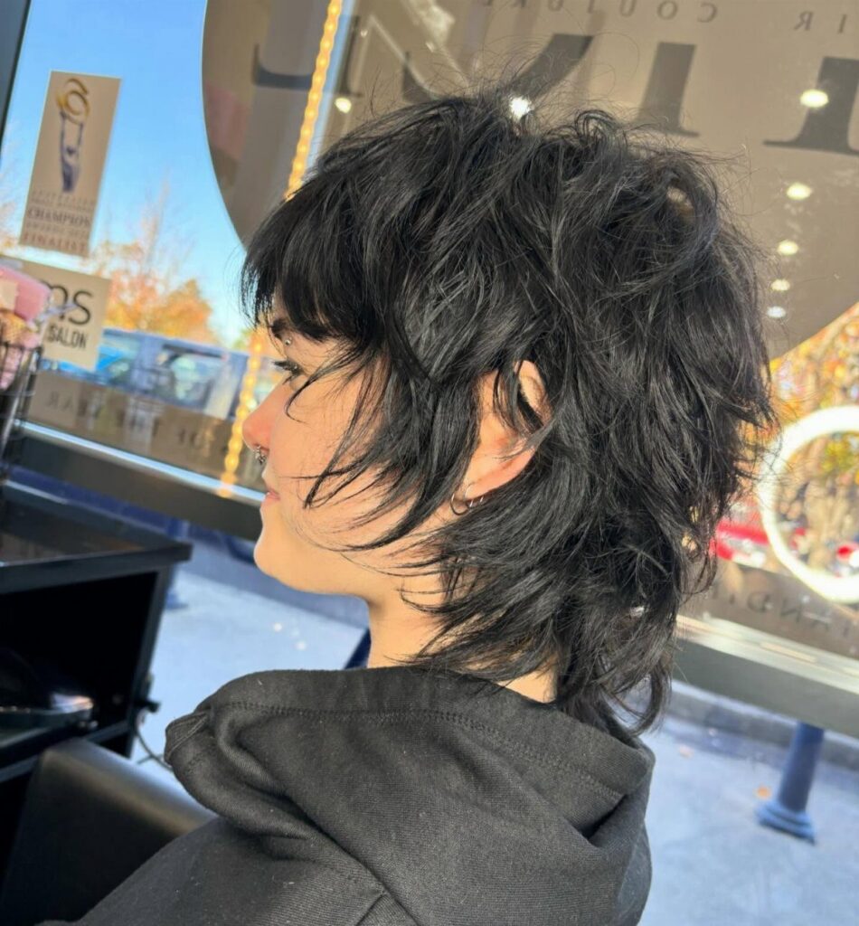 Side-profile person showing a shaggy dark pixie haircut with tousled bangs