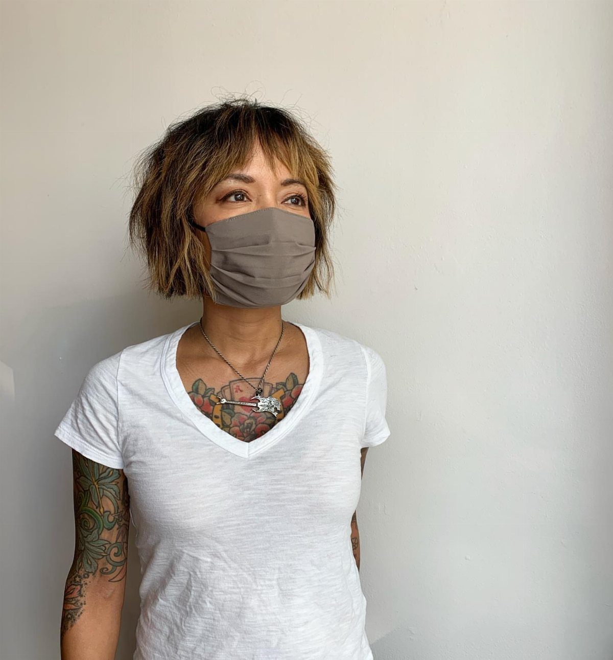 Woman wearing mask with messy short layered brown bob haircut and visible tattoos