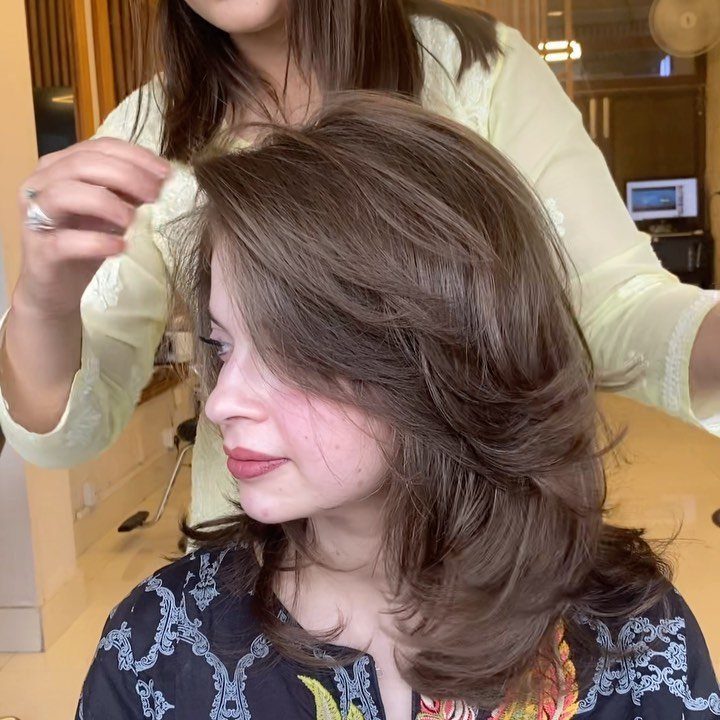 Woman with shoulder-length layered brown hair and sweeping bangs in a salon