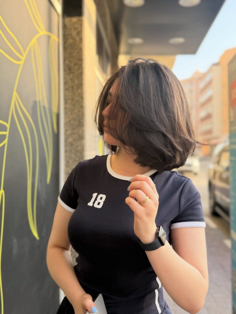 Dark shoulder-length bob frames a person’s face as they stand beside a mural