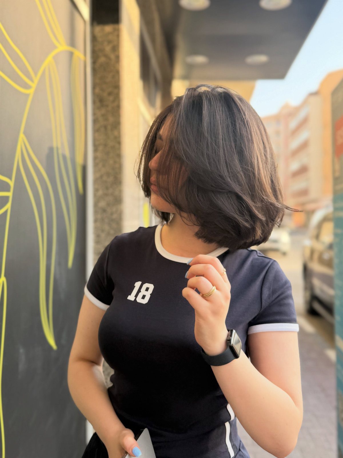 Dark shoulder-length bob frames a person’s face as they stand beside a mural